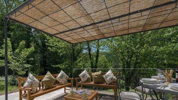 An outdoor patio with a wooden sofa set, a small table, and a metal dining table with chairs. - Belvilla by OYO Villa Arnia (Reggello)
