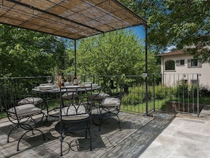An outdoor patio with a round table set for dining, surrounded by metal chairs with cushions.
