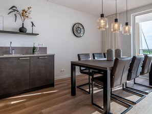 Eine moderne Küche mit dunkler Arbeitsplatte, einem Essbereich mit Holztisch und -stühlen sowie einem großen Fenster, das für natürliches Licht sorgt.