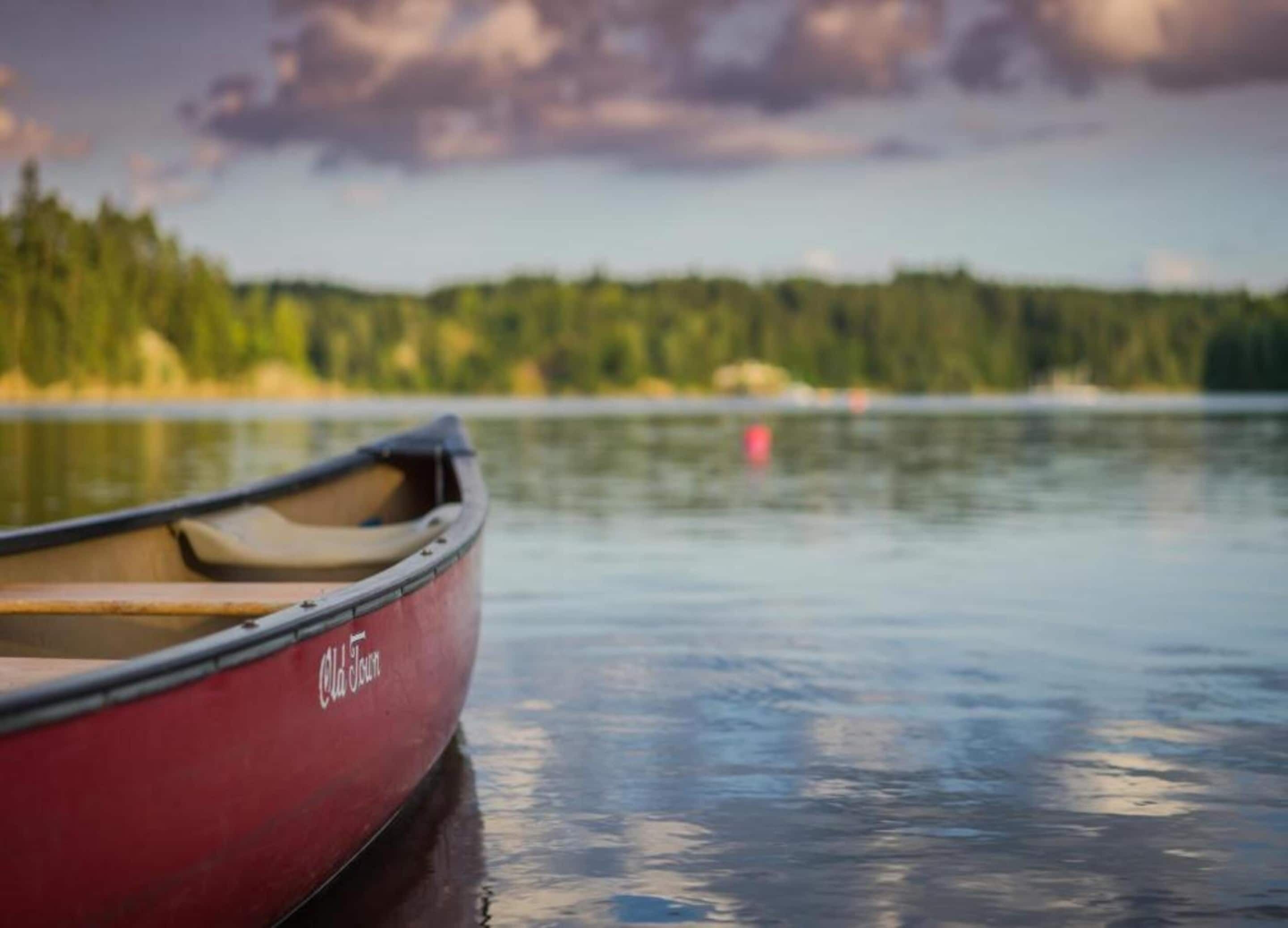 A red canoe with "Old Town" written on it, floating on calm water with a forested shoreline in the background.