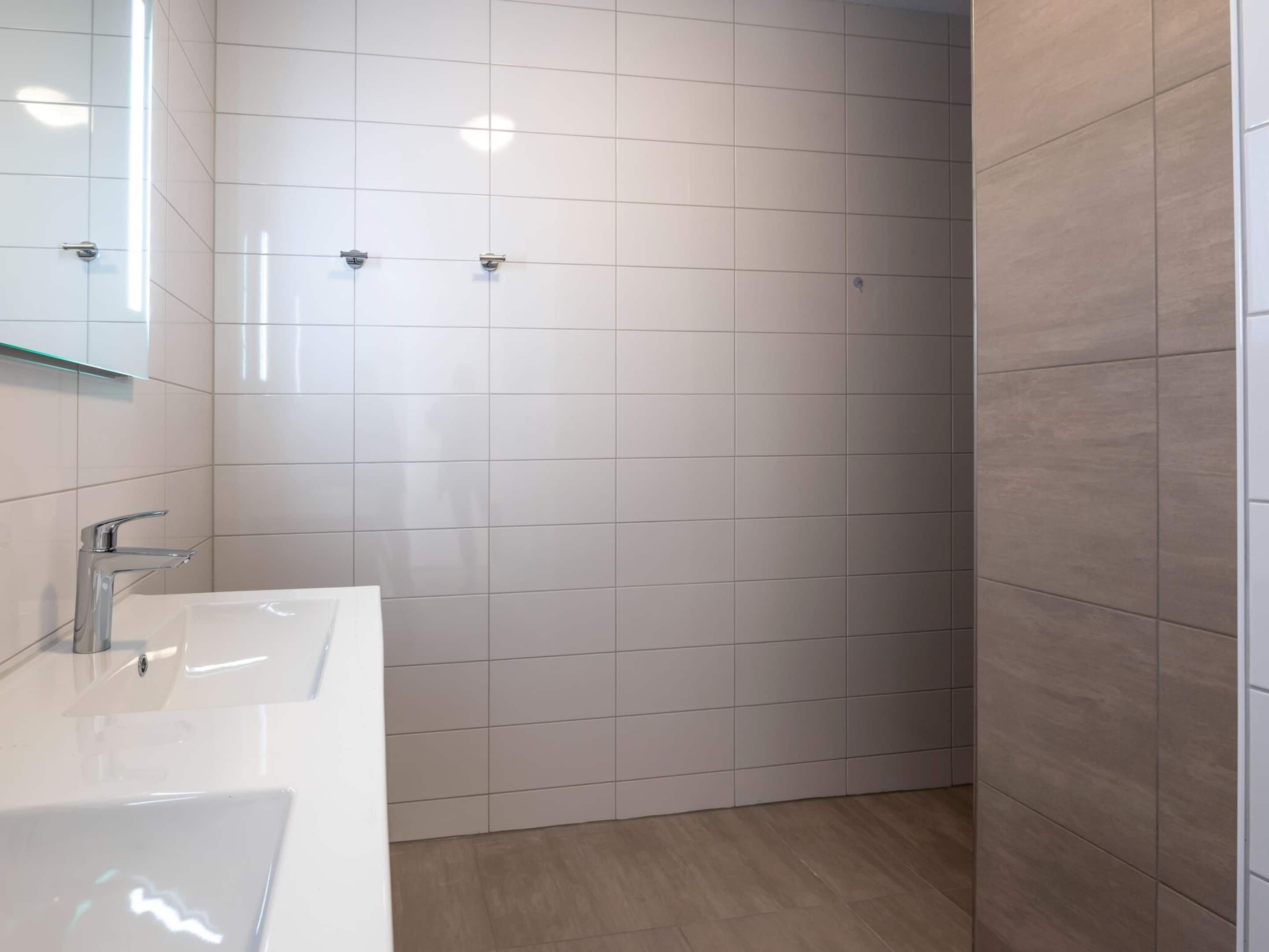 A modern bathroom with a white sink, a mirror, and a shower area.