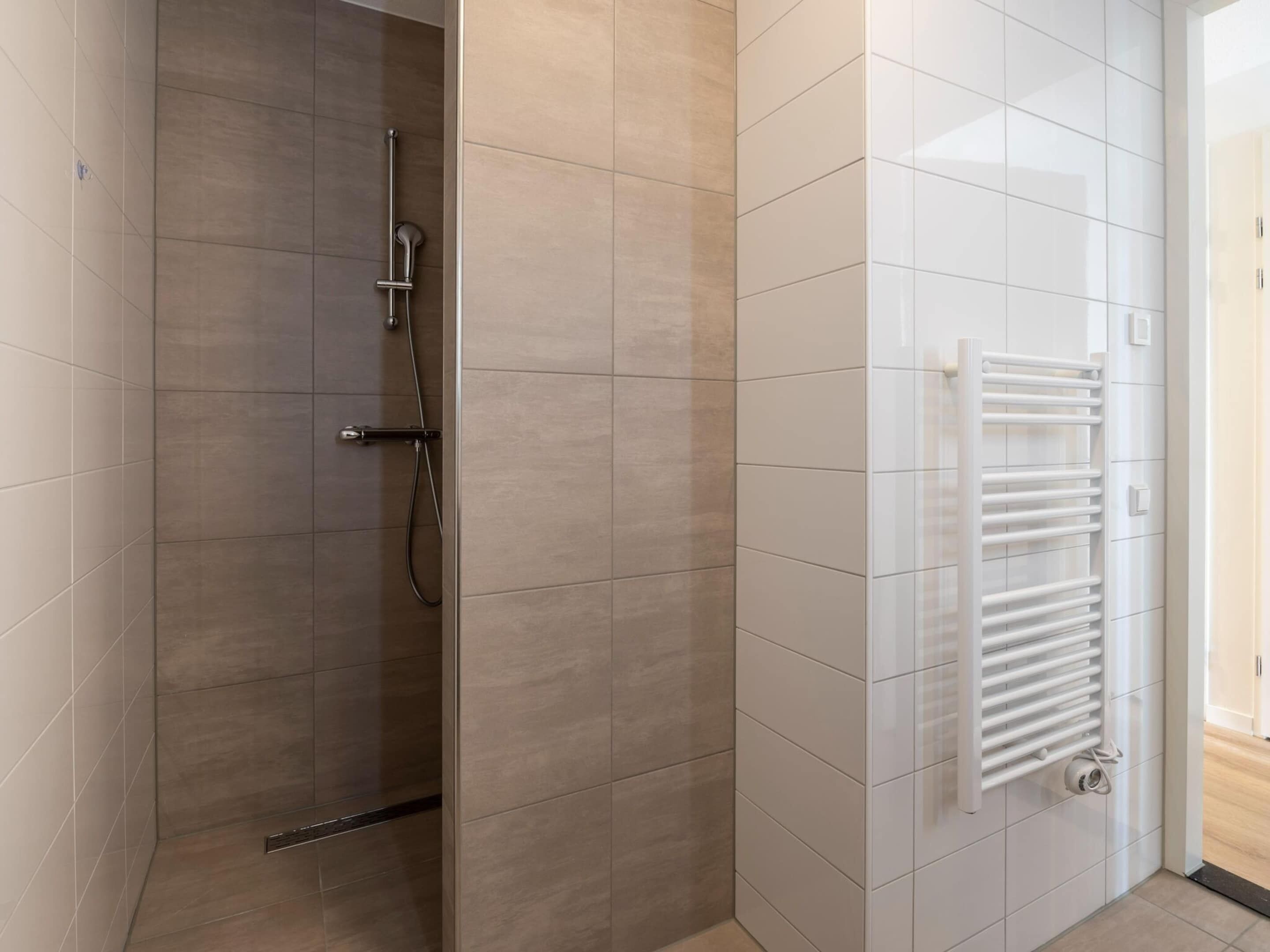 A modern bathroom with a glass-enclosed shower, a white tiled wall, and a built-in white towel rack.