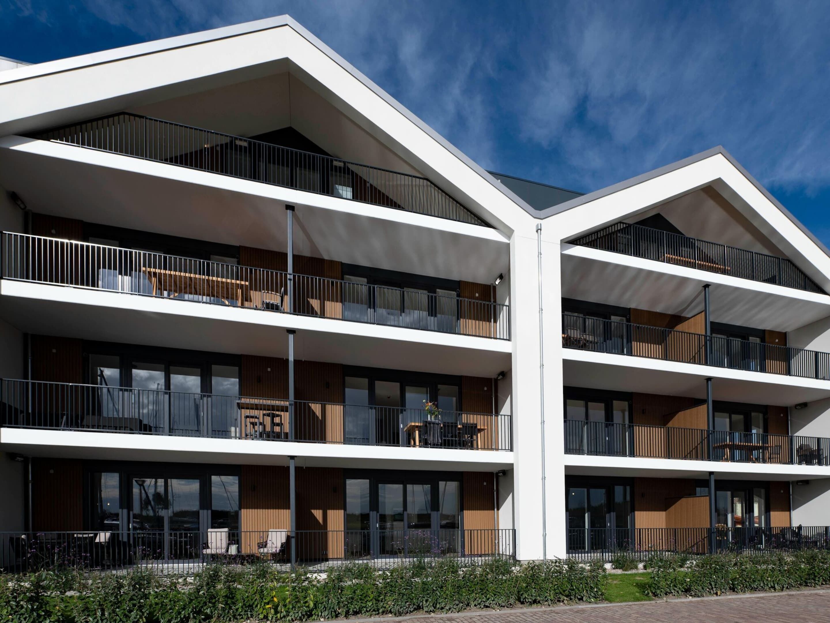 Een modern meerlaags gebouw met balkons, grote ramen en een plat dak.