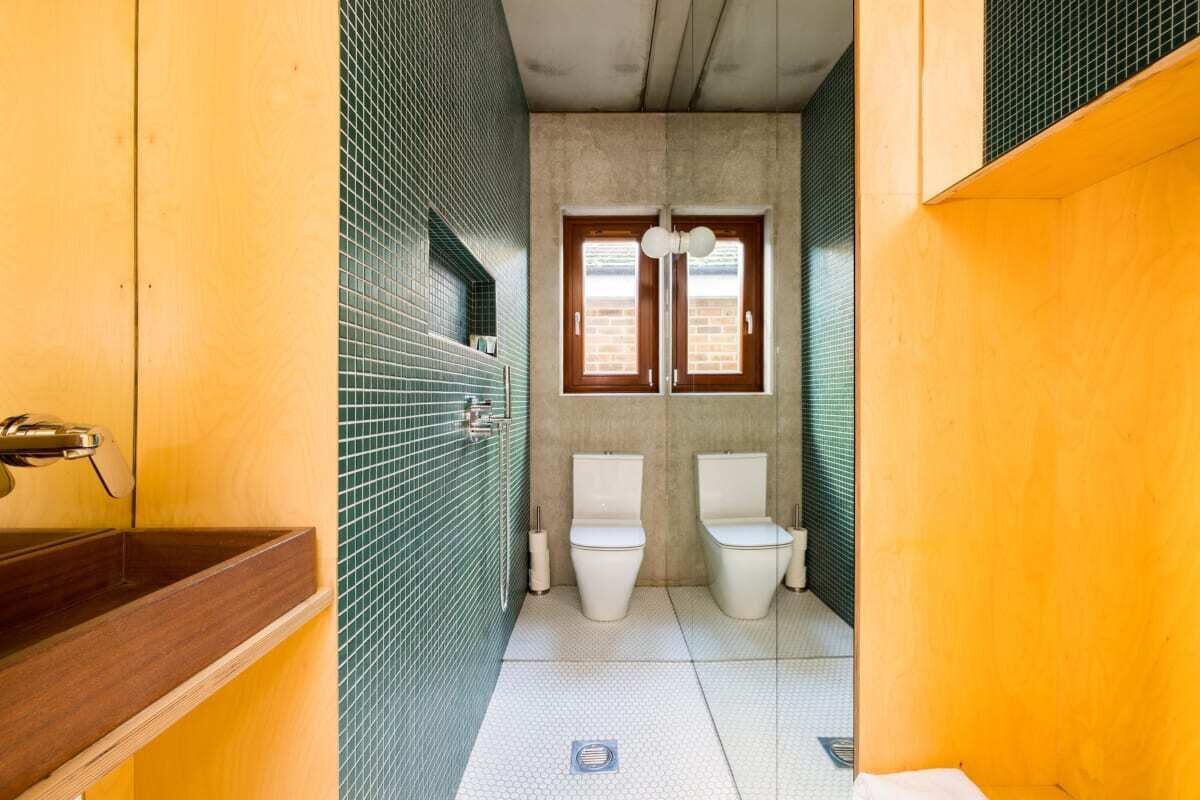 A compact bathroom with two toilets, a sink, and a window.