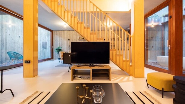 A modern living room with a wooden staircase, a flat-screen TV, and a glass coffee table. - The Victoria Park Sanctuary - Stunning 2bdr Flat (London)