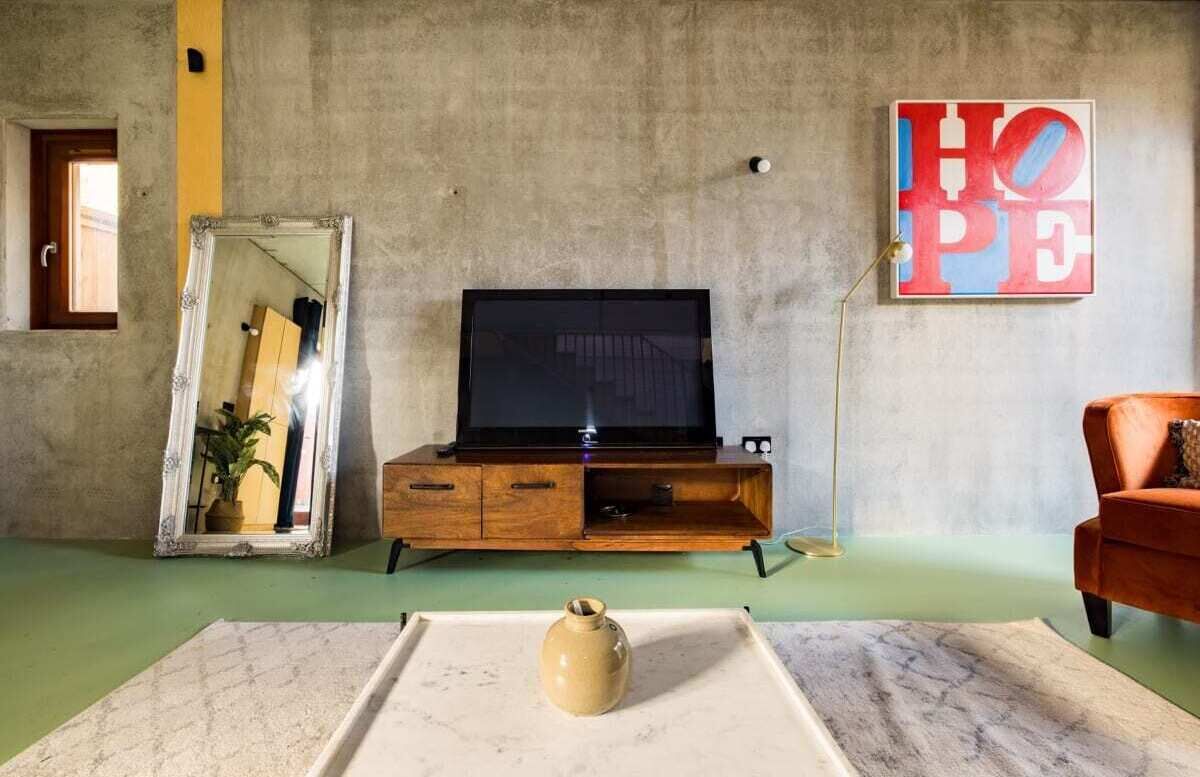 A living room with a television on a wooden stand, a large mirror, a vase on a table, and a 'HOPE' painting on the wall.