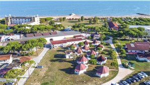 An aerial view of a coastal town with a beach, a castle-like structure, and several white buildings with red roofs. - Cozy apartment in Cavallino-Treporti (Cavallino-Treporti)