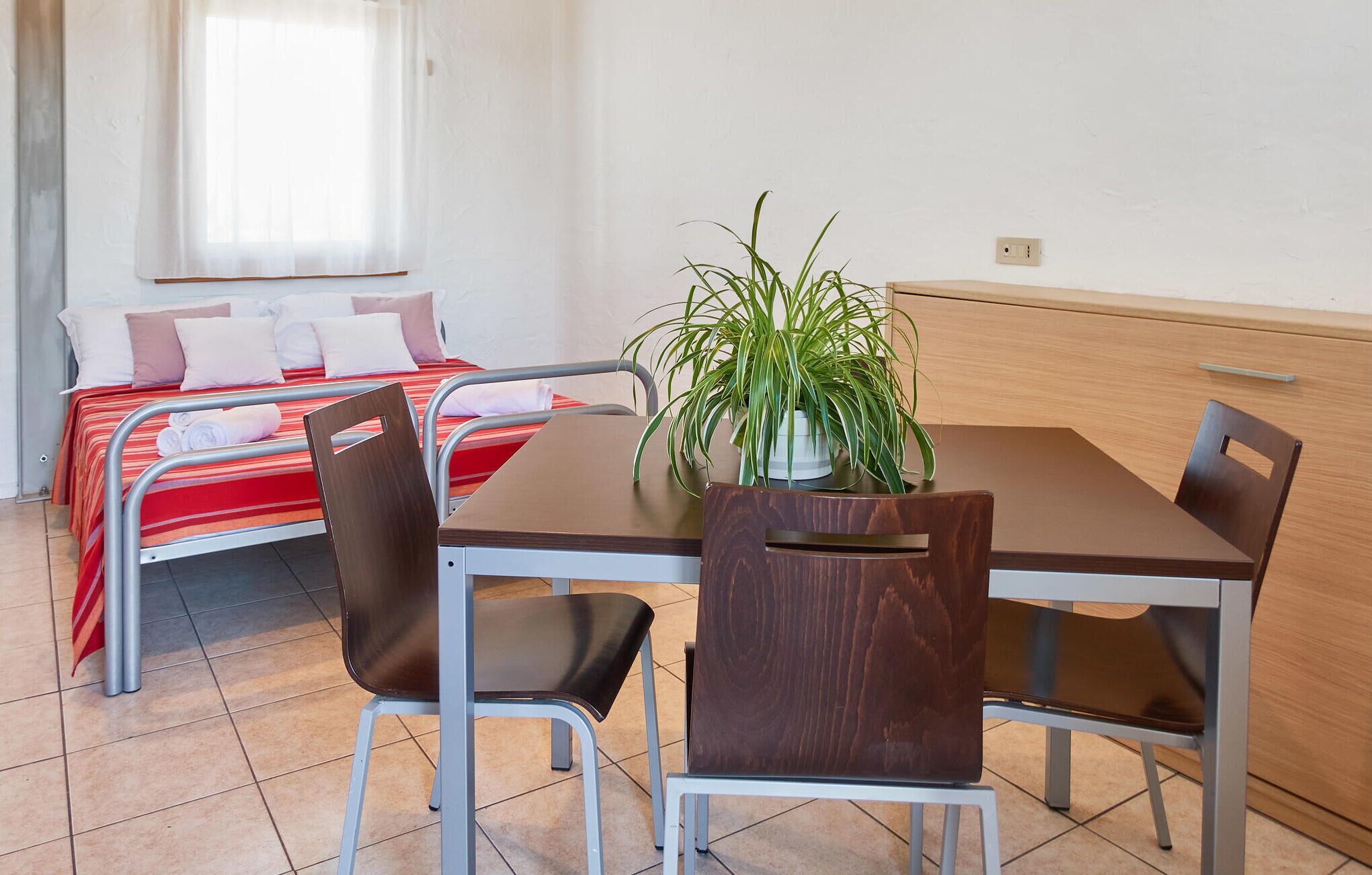 Habitación de hotel con cama, una mesa de comedor con sillas, una planta en maceta y un armario de madera.