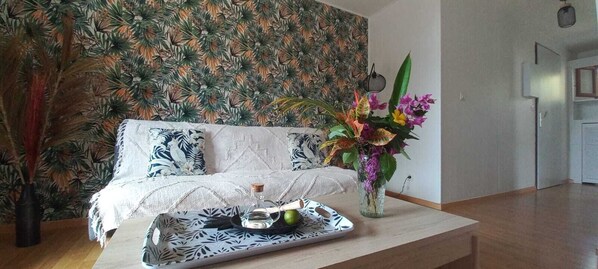 A living room with a patterned wallpaper, a white sofa, a coffee table with a tray, and a vase with flowers.