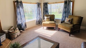 A living room with two armchairs, a glass coffee table, and a view of a grassy area through large windows with patterned curtains. - Country paradise! Close to Telluride (Norwood)