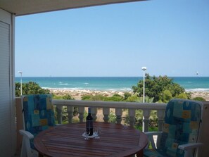 A wooden table with two chairs on a balcony overlooking a beach.