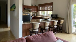 A modern kitchen with a central island, bar stools, and a dining area with a sofa. - Stay on the Beach at Acqua Condo (Puntarenas Province)