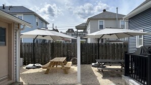 A backyard with two picnic tables, a wooden fence, and houses in the background.