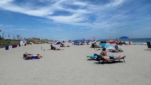 A beach with people sunbathing and relaxing. There are umbrellas and beach chairs.