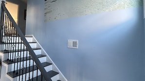 A staircase with black railings and white steps, leading to a room with a blue wall and a beach mural.