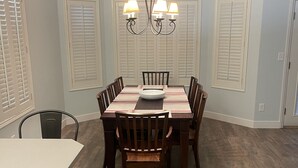 Un coin repas avec une table et des chaises en bois, un lustre et un ventilateur de plafond blanc.