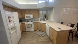 Une cuisine compacte équipée d’un four à micro-ondes, d’une cuisinière et d’un lave-vaisselle. On y trouve un petit îlot central avec un évier et une chaise. La cuisine est dotée de meubles en bois et d’un plancher de couleur claire.