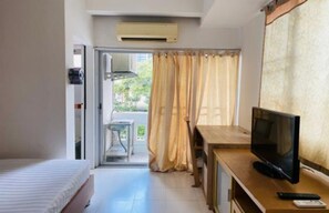 A hotel room with a bed, a desk with a TV, a window with curtains, and an air conditioning unit. - Grandview Place (Bangkok)