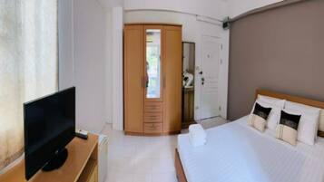 A hotel room with a bed, a TV on a wooden dresser, a wardrobe, and a door leading to another room.