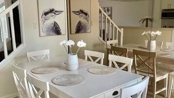 A dining area with a white table and chairs, two framed bird paintings on the wall, and a vase with flowers on the table.