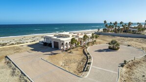 A beachfront property with a paved walkway, palm trees, and a building with a white facade. - Beachfront Hacienda on the Sea of Cortez with pool near Four Seasons Resort (La Ribera)