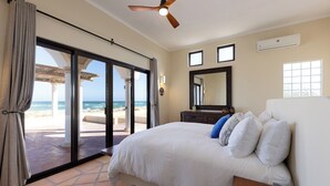 A bedroom with a large bed, a ceiling fan, a dresser, and a view of the beach through a sliding glass door. - Beachfront Hacienda on the Sea of Cortez with pool near Four Seasons Resort (La Ribera)