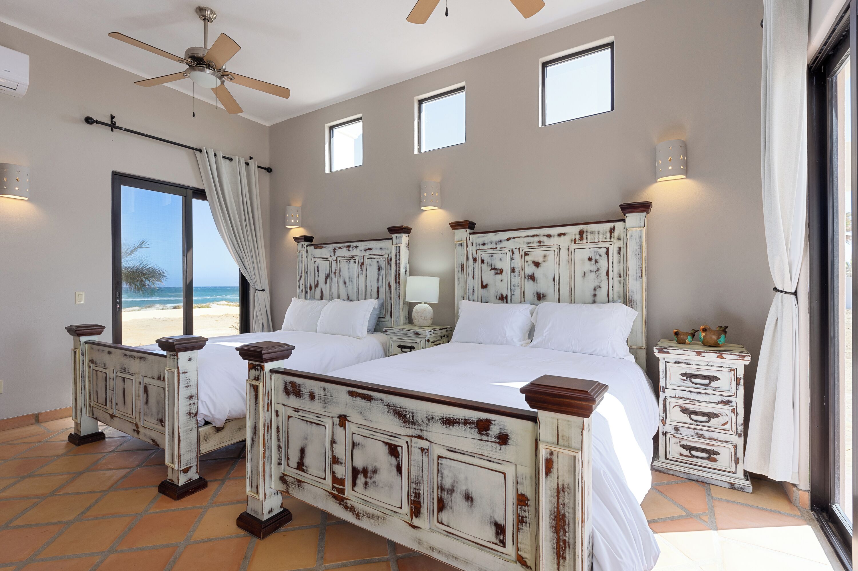 Een slaapkamer met een groot bed, een plafondventilator en uitzicht op het strand.