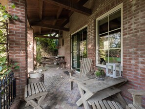 Une terrasse couverte, dotée de meubles en bois, de murs en briques et offrant une vue sur l’extérieur.