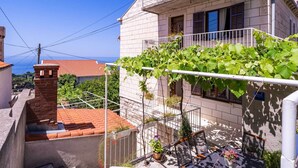 A residential building with a balcony, a brick chimney, and a view of the sea. - Apartments Stella - One Bedroom Apartment With Terrace A1 (Dubrovnik)