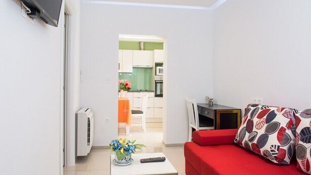 A modern living room with a red sofa, a small white table with a vase of flowers, and a TV mounted on the wall. - Apartments Stella - One Bedroom Apartment With Terrace A1 (Dubrovnik)