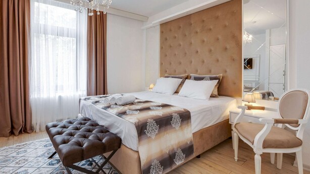 A bedroom with a large bed, a tufted headboard, a bedside table with a lamp, a chair, and a patterned rug. - Cozy Corner in Oberhausen (Oberhausen)