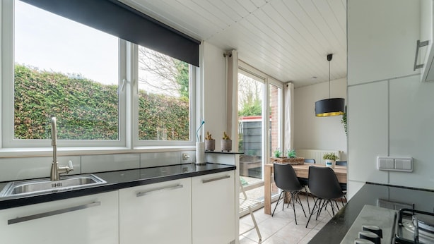 A modern kitchen with a large window, a dining area with a table and chairs, and a gas stove. - Holiday Home in Zeeland Near Lake (Baarland)