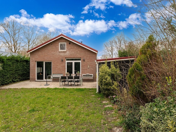 Ein Ziegelhaus mit Terrasse, überdachtem Bereich und gepflegtem Rasen.