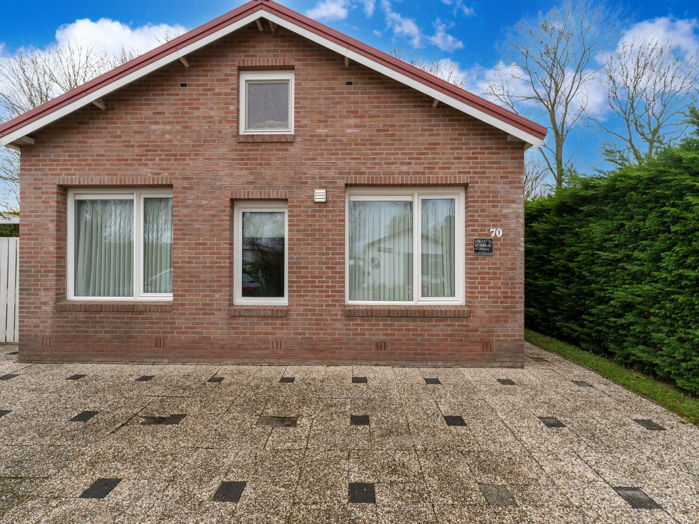 Une maison à deux étages, construite en briques et coiffée d’un toit rouge, avec trois fenêtres et une allée gravillonnée.