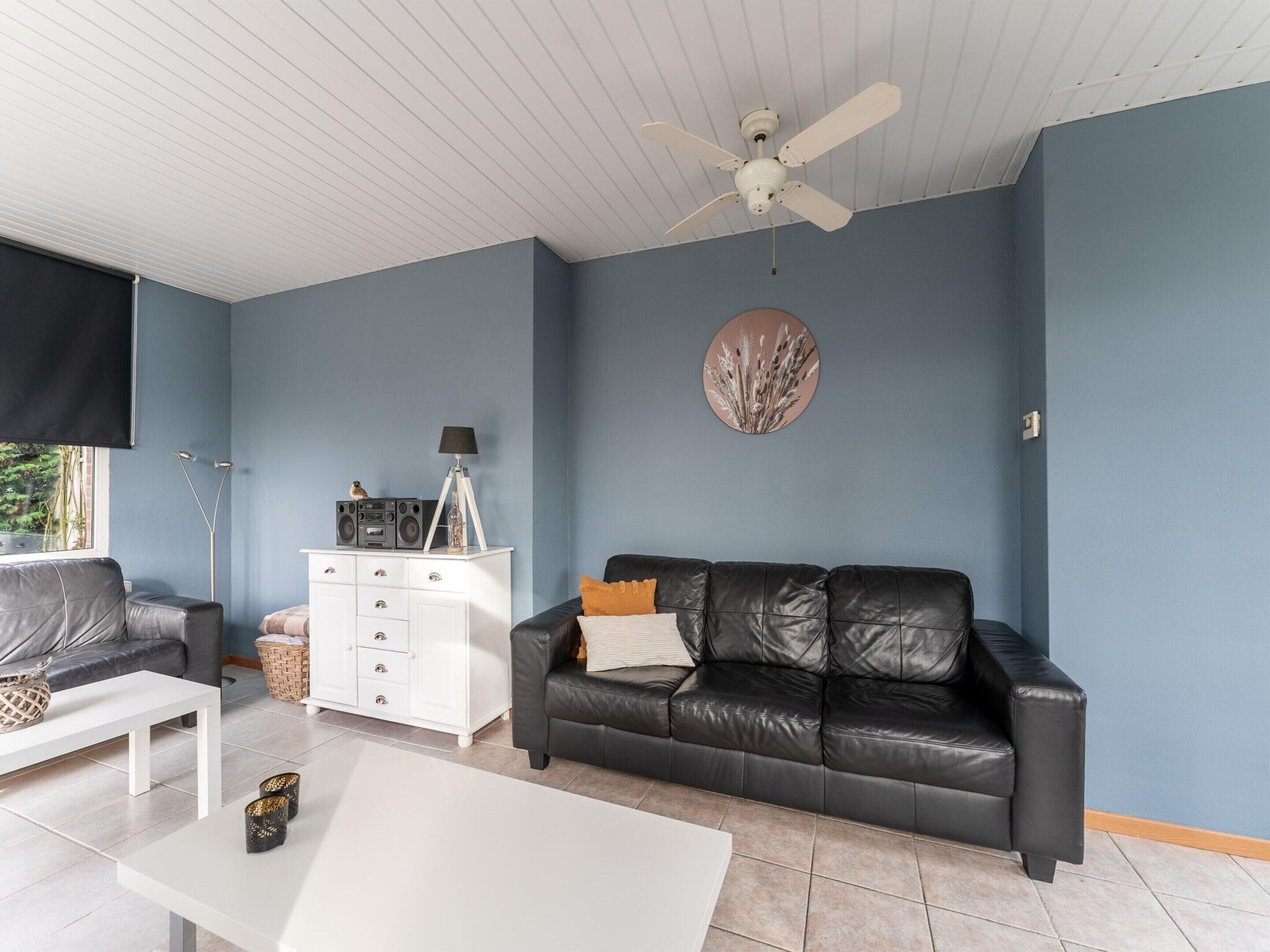 A living room with a black leather sofa, a white coffee table, a white cabinet, and a ceiling fan.