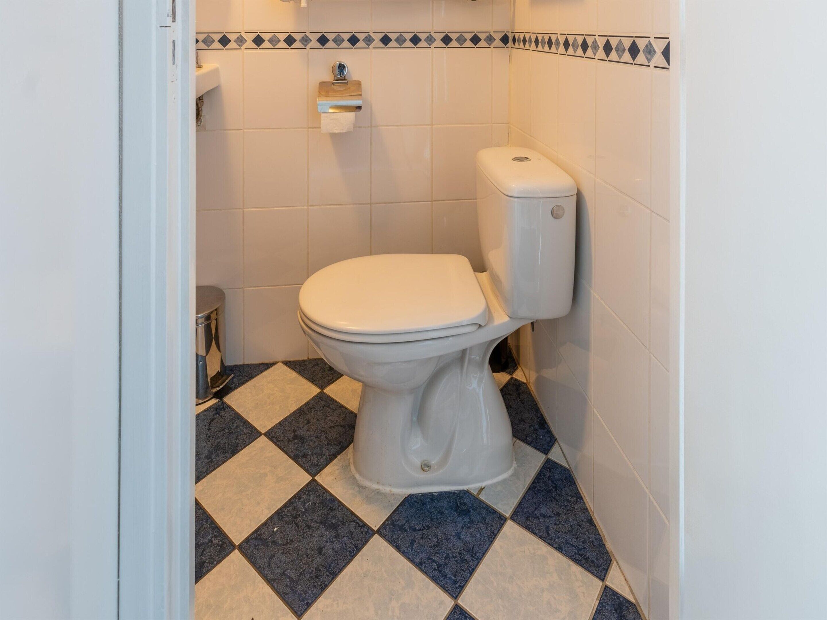 Ein kleines Badezimmer mit Toilette, Mülleimer und Toilettenpapierhalter an der Wand.