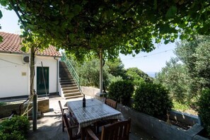 Eine Terrasse mit Tisch und Stühlen, eine Treppe zu einem Gebäude und umgebende Bepflanzung.