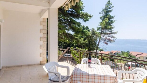 A balcony with a table and chairs, overlooking a coastal area with trees and houses. - Holiday Home Blue Vineyard- Three Bedroom House With Terrace and Sea View (Orebic)