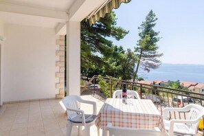 A balcony with a table and chairs, overlooking a coastal area with trees and houses. - Holiday Home Blue Vineyard- Three Bedroom House With Terrace and Sea View (Orebic)