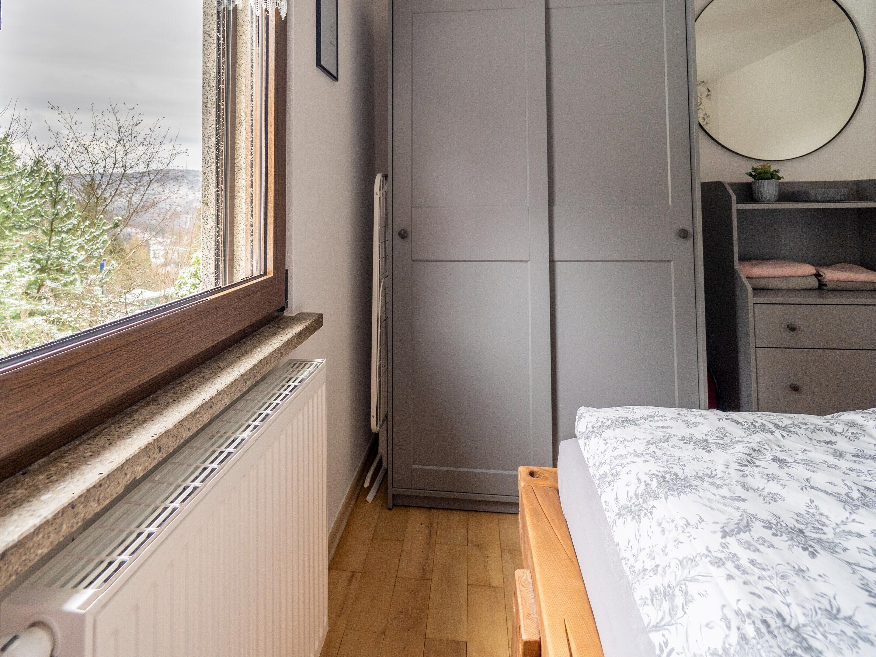 Une chambre à coucher comprenant un lit, une armoire, un radiateur, une fenêtre et un miroir.