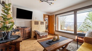 Una sala de estar acogedora con una mesa de centro de madera, un televisor montado en la pared y un ventanal con vistas a árboles cubiertos de nieve.