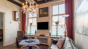 A living room with a sofa, a coffee table, a chandelier, a flat-screen TV, and a large window with curtains. - Lovely Holiday Home From 1761 With Contemporary Comfort (Bad Nieuweschans)