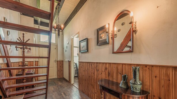 A wooden-paneled hallway with a staircase, a wooden table with decorative items, and a mirror on the wall. - Lovely Holiday Home From 1761 With Contemporary Comfort (Bad Nieuweschans)