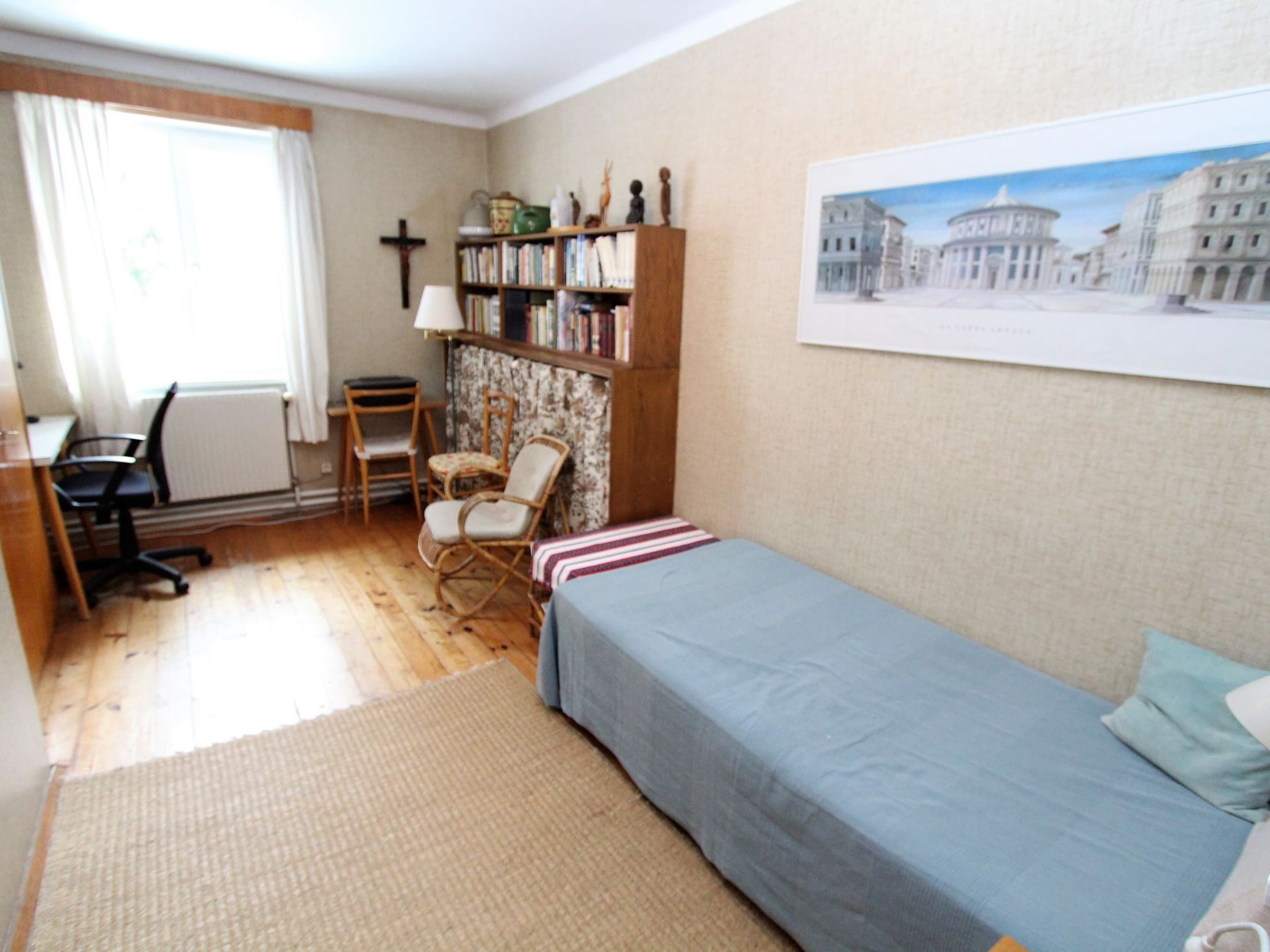 A small, tidy bedroom with a single bed, a desk, a chair, and a bookshelf.
