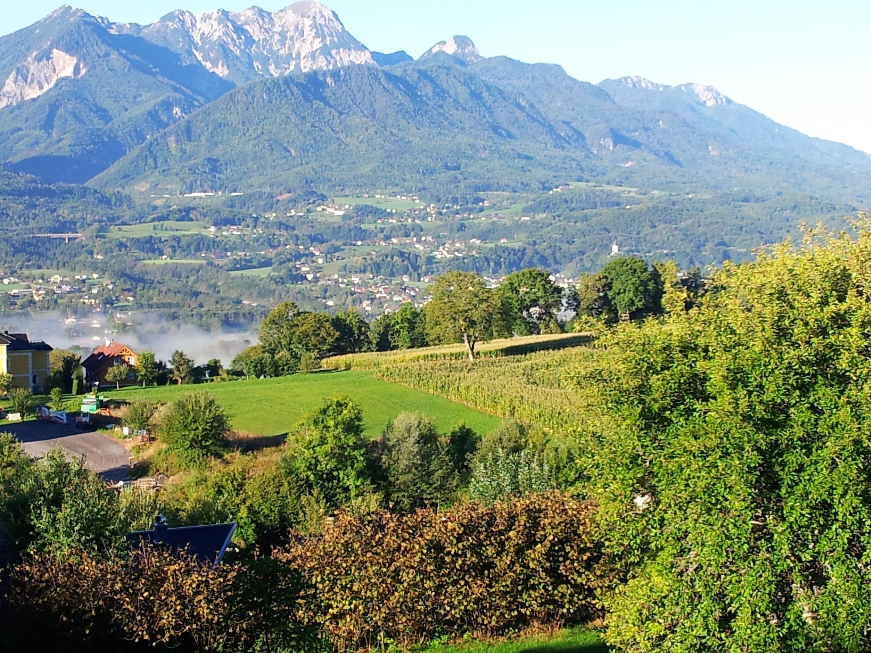 Un paysage rural avec un village, des champs verdoyants et des montagnes en arrière-plan.