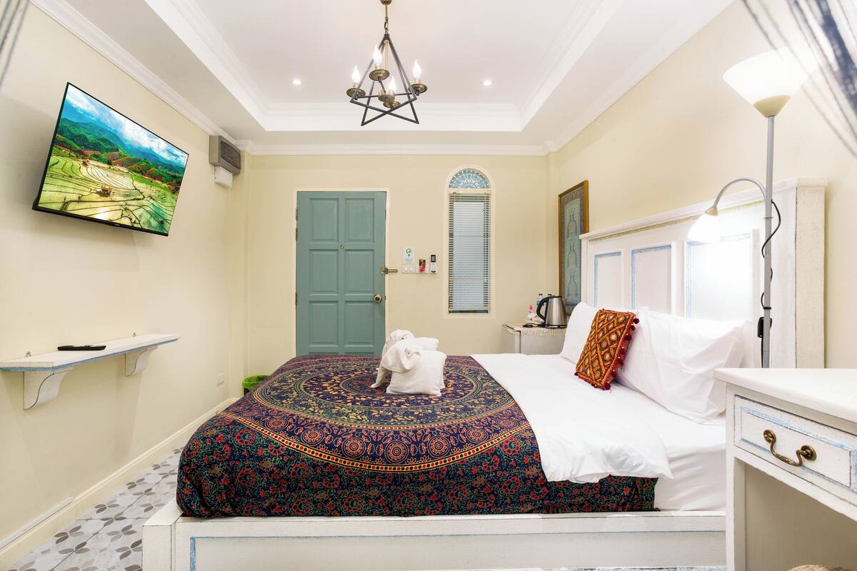 A bedroom with a bed, a television, a chandelier, a door, and a window.