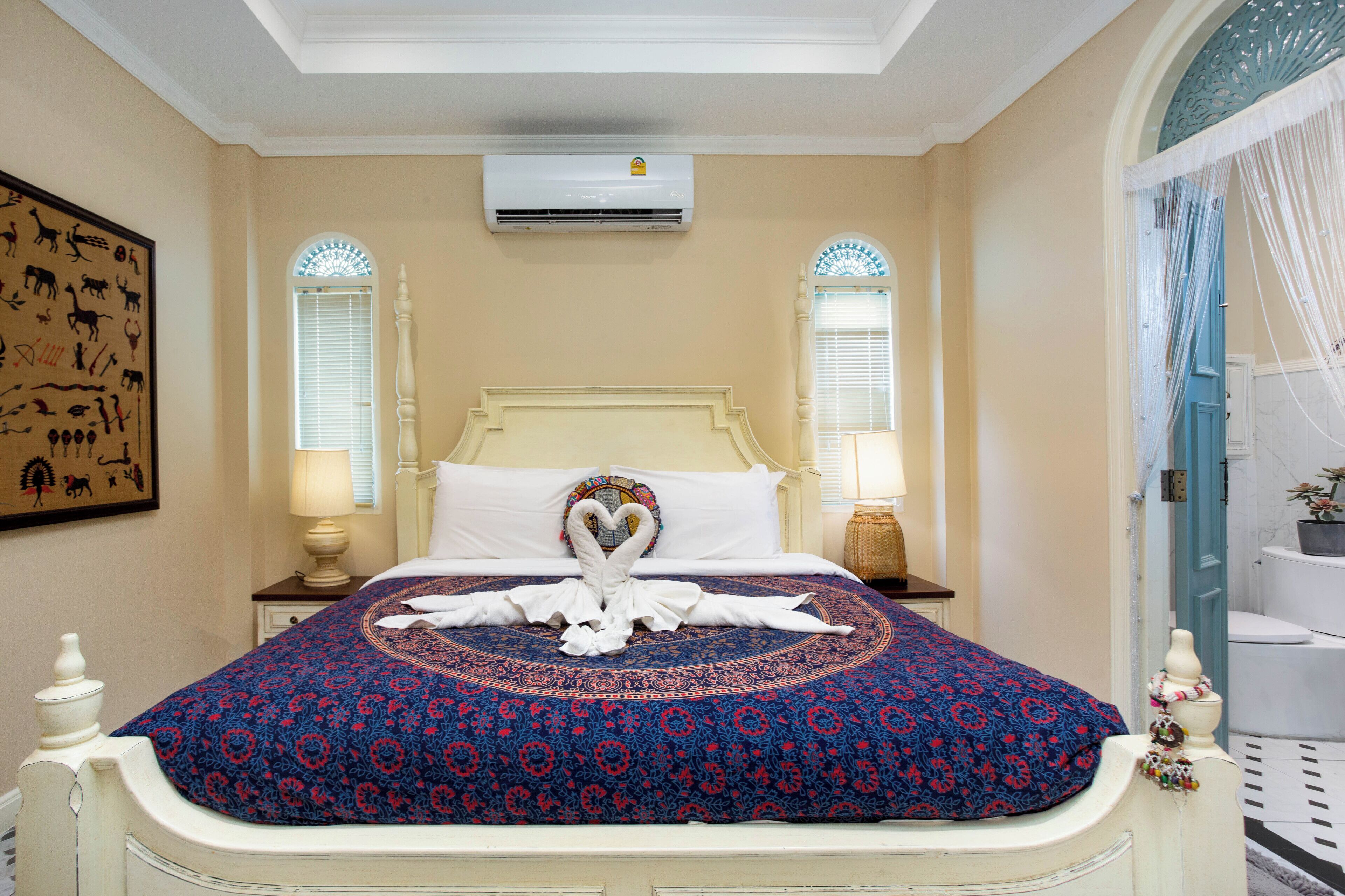 Una cama con una toalla dispuesta en forma de corazón, un edredón estampado y un aire acondicionado de pared.