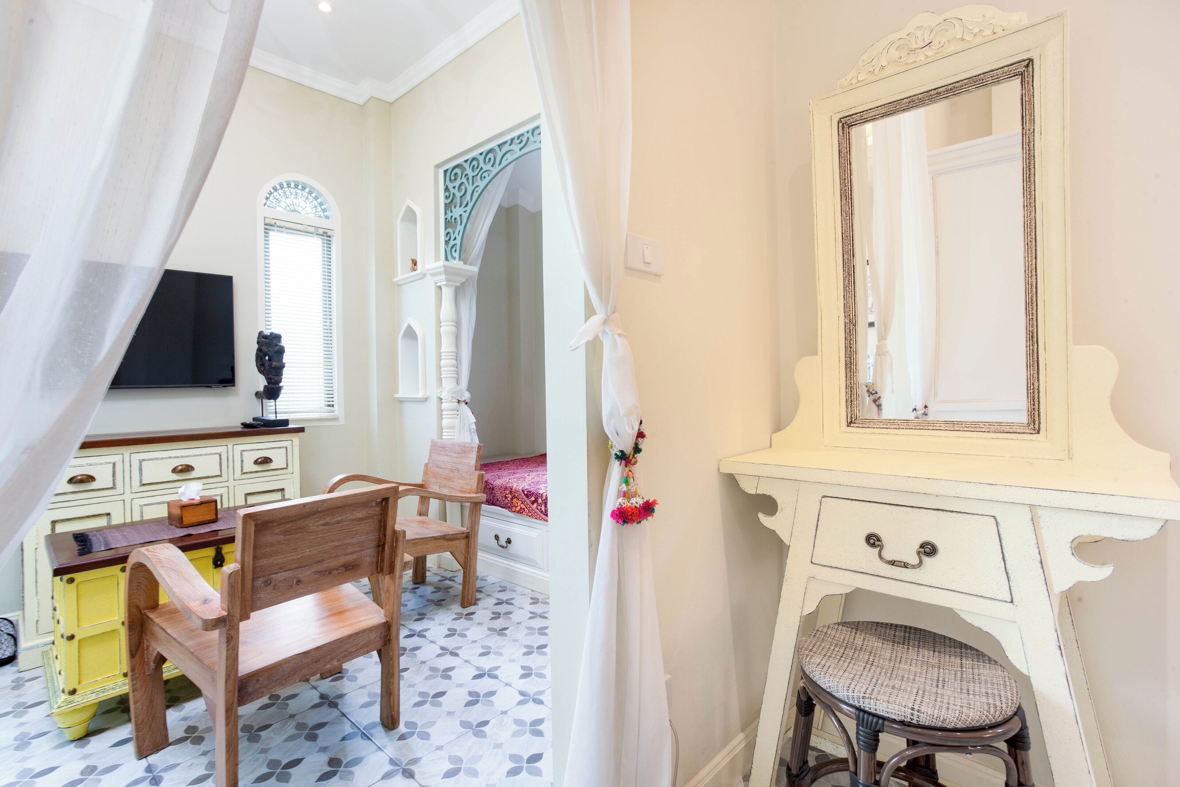 A bedroom with a wooden bed, a white vanity with a mirror, a wooden chair, and a yellow dresser.