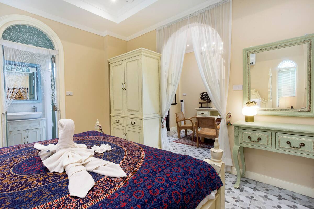 A hotel room with a bed, a wardrobe, a vanity with a mirror, and a bathroom with a sink and shower.