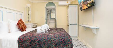 A bedroom with a bed, a TV, a wardrobe, and a bathroom visible through an arched doorway.